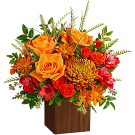 Orange and red floral arrangement in a wooden cube vase