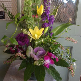 Tall mixed floral arrangement with yellow lilies, purple blooms, and green accents in a vase