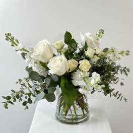 White roses and white blooms in a clear glass vase with greenery
