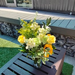 Yellow roses and white flowers arranged in a glass vase