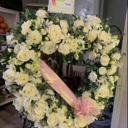 Heart-shaped white floral wreath with a pink ribbon and bow