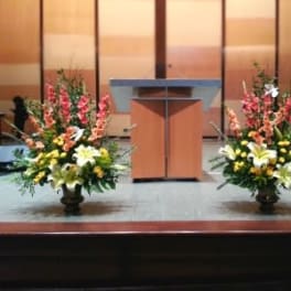 Two large floral arrangements flank a podium on a stage.