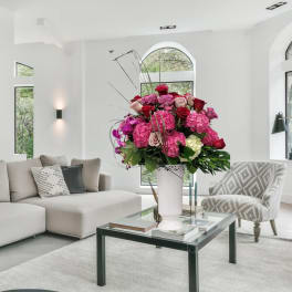 Large pink and red floral arrangement in a white vase on a coffee table