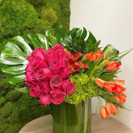 Pink roses and orange tulips arranged in a green glass vase
