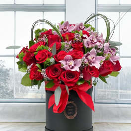 Red roses and pink orchids in a black hatbox with a red ribbon