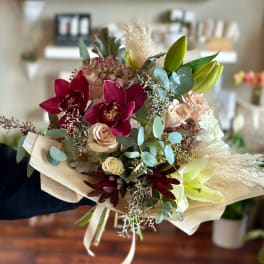 Bouquet of burgundy orchids, pale roses, and lilies wrapped in paper