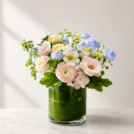 Pastel bouquet of roses, ranunculus, and blue blooms in a glass vase