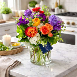 Colorful bouquet of roses and purple blooms in a glass vase