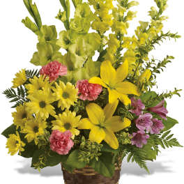 Yellow mixed flower arrangement in a woven basket with pink accents