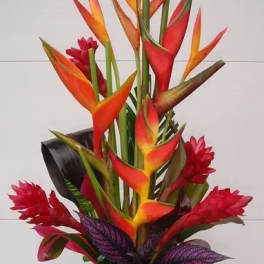 Tropical bouquet with orange and red heliconia in a gold vase