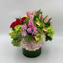 Mixed bouquet with pink tulips, roses, hydrangea, and green orchids in a green vase