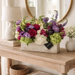 Mixed bouquet of roses, hydrangeas, and purple blooms in a rustic wooden box
