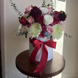 Bouquet of pink, red, white, and burgundy flowers in a white hat box with a red ribbon