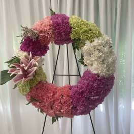 Circular floral wreath on a black stand with pink, purple, green, and white blooms