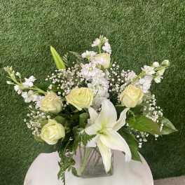 Bouquet of pale yellow roses and white lilies in a square glass vase
