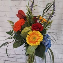 Mixed bouquet in a clear glass vase with red, yellow, orange, and blue flowers