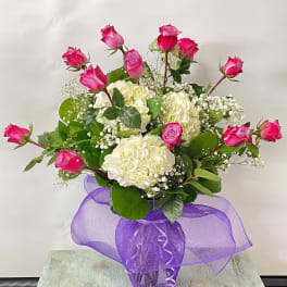 Pink roses and white hydrangeas in a glass vase with purple ribbon
