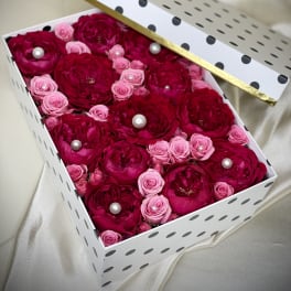 Box of red and pink roses with pearls arranged in a white polka dot gift box with lid