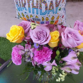 Birthday balloon above a bouquet of roses and pink flowers in a glass vase