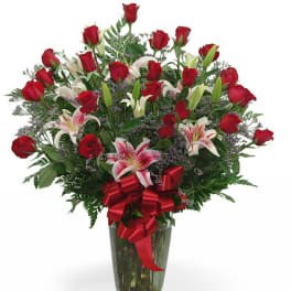 Bouquet of red roses and pink lilies in a glass vase with a red ribbon