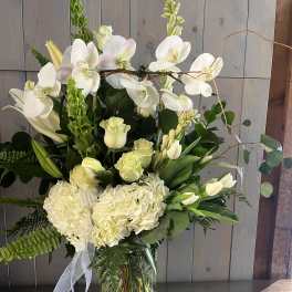 White orchids and pale flowers arranged in a clear glass vase with a ribbon.