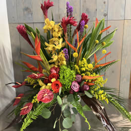 Tropical floral arrangement with orchids, roses, and bird-of-paradise in a low container
