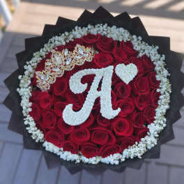 Round bouquet of red roses with white floral initials and a jeweled crown