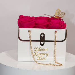 Hot pink roses arranged in a white purse-style box with gold chain and butterfly accent.