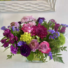 Mixed bouquet of pink, purple, and yellow flowers in a glass vase
