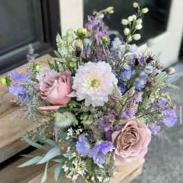 Pastel bouquet of roses, dahlias, and purple blooms in a glass vase