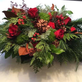 Red roses in a holiday arrangement with pinecones and evergreen branches
