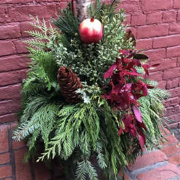 Holiday greenery arrangement with a pinecone and red ornament on a birch log