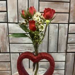 Red roses and white filler flowers in a glass tube vase with a glittery heart base