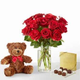 Red roses in a glass vase with a teddy bear and chocolates