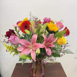 Mixed bouquet of pink lilies, roses, and bright gerbera daisies in a pink vase