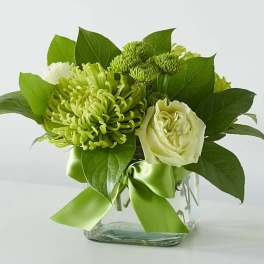Green and white floral arrangement in a clear glass vase with a ribbon