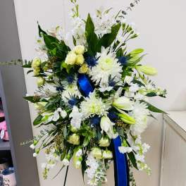 Large white floral standing spray with blue ribbon on an easel