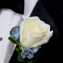 White rose boutonniere with small blue flowers on a black suit lapel