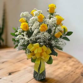 Yellow roses with white baby's breath in a glass vase tied with a yellow ribbon.