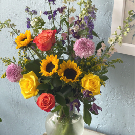 Mixed bouquet of sunflowers, roses, and purple flowers in a glass vase