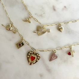Gold charm necklaces with heart and arrow pendants on a marble surface