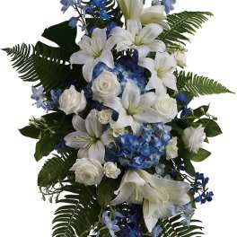 Standing floral spray with white lilies, white roses, and blue flowers on an easel