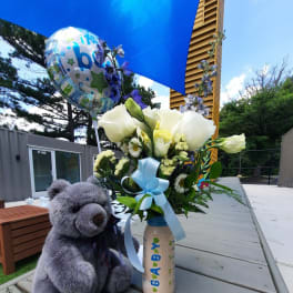 Bouquet of white and pale yellow flowers in a decorated bottle with a teddy bear and baby balloon