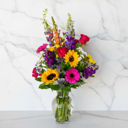 Colorful mixed bouquet in a clear glass vase with sunflowers and roses