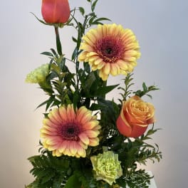 Mixed bouquet with orange roses, pink-yellow gerbera daisies, and green carnations in a yellow vase