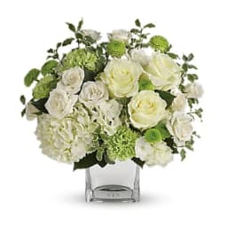 White roses and green blooms in a clear square vase