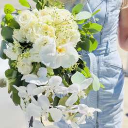 White bouquet with roses and orchids held by a person in a light blue dress