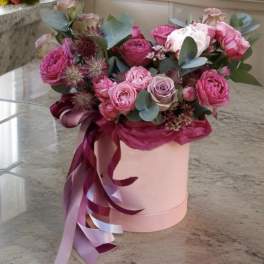 Pink and lavender roses in a round hatbox with ribbon