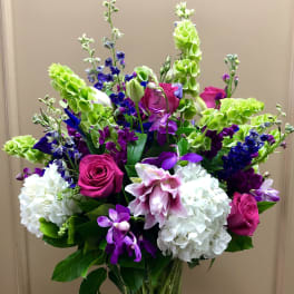 Tall mixed bouquet with pink roses, white hydrangeas, and purple orchids in a glass vase
