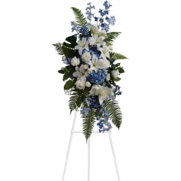 Tall standing spray of white lilies and roses with blue delphinium and hydrangea on a white easel